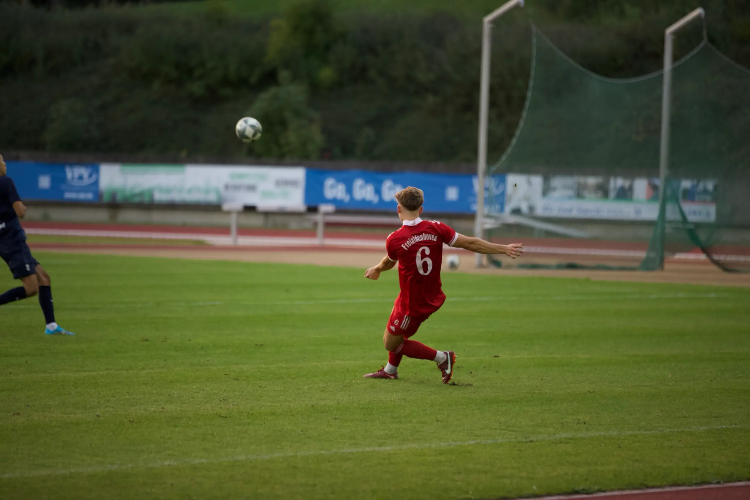 Fußballspieler im roten Trikot schlägt einen Ball auf dem Platz